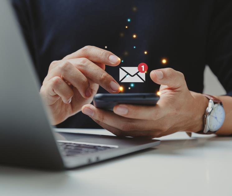 Person using a phone and a laptop with an email icon overlay