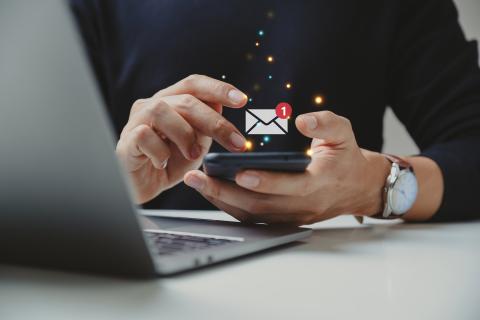 Person using a phone and a laptop with an email icon overlay